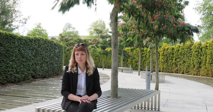 a beautiful girl with long hair in a business suit is sad sitting in a park on a bench. failure. longing. Business Challenges.
