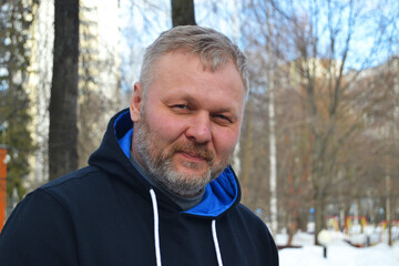 A man with a gray beard on the street in winter looks at the camera