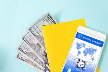 Close up blank yellow piece of paper, 100 dollar bills and digital health passport app in mobile phone on blue background.