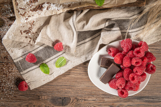 Ripe sweet raspberries and chocolate in a plate on wooden table. Close up, top view, high resolution product