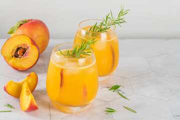 Healthy summer juice - peach cocktail with ice, rosemary twig, sugar rim, fruit slices in misted glass in elegant white interior on white marble countertop. Closeup.