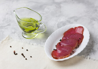 Delicious slices of cold smoked tuna on a white plate, olive oil and a concrete background. Fresh seafood. Selective focus.