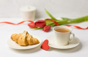A cup of tea with a croissant, delicate flowers, a sugar bowl in the background. Birthday greeting card, wedding. Morning breakfast.