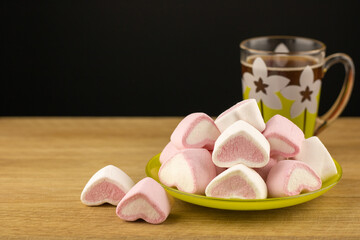 Colored marshmallows sweets in the saucer on around wooden textured background. A cup of aromatic...