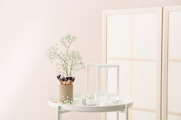 Cosmetic products, makeup brushes, flowers and empty picture frames on table in room