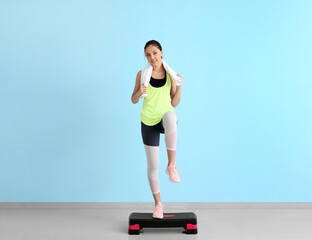 Sporty teenage girl with aerobic stepper near blue wall
