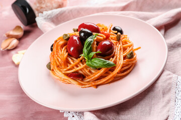 Plate with tasty Pasta Puttanesca on pink background