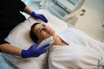Overhead view of a middle aged Caucasian woman receiving a facial laser treatment in a wellness spa clinic. Cosmetology, dermatology, beauty treatment and body care concept