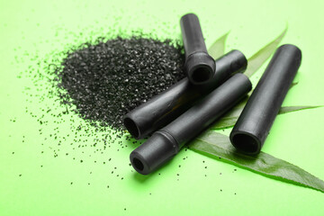 Heap of activated carbon powder and black bamboo sticks on green background