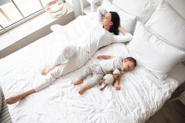 Young mother and her adorable baby with toy sleeping on bed
