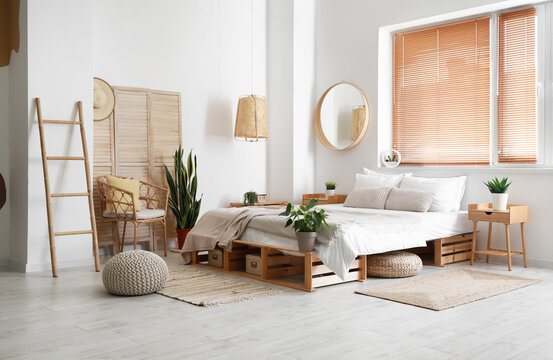 Interior of light bedroom with comfortable bed, chair and houseplants