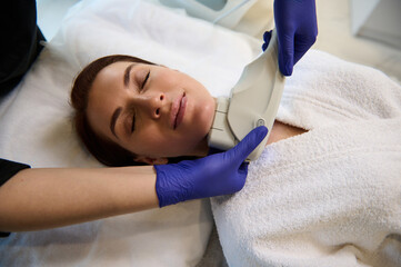 Top view of young European beautiful woman getting facial treatment in modern wellness spa using...