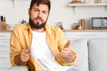 Handsome young man with cup of tea video chatting in kitchen