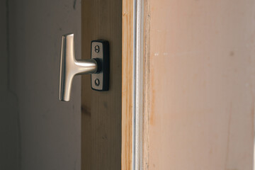 Typical window knob mounted on a wooden window frame in closed position. Metal contemporary modern knob or hook for opening the window.