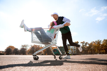 Young man riding his girlfriend in shopping cart outdoors