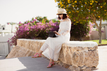 Pretty young girl using tablet while sitting near a tropical resort during summer vacation. Touch on screen and communicate. Relaxing on clean fresh morning air and reading e book on touch pad