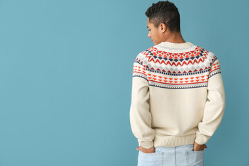 Handsome African-American guy in knitted sweater on color background