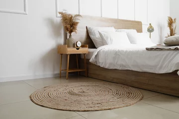 Foto op Canvas Comfortable bed, wicker rug and nightstand table with dry reeds near white wall © Pixel-Shot