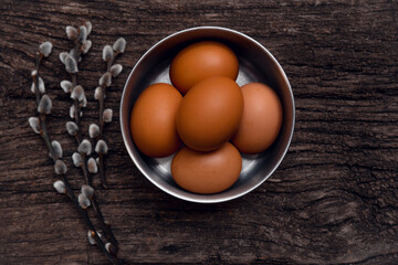 Happy easter composition.Top view chicken eggs in a metal bowl on a wooden background with willow branches