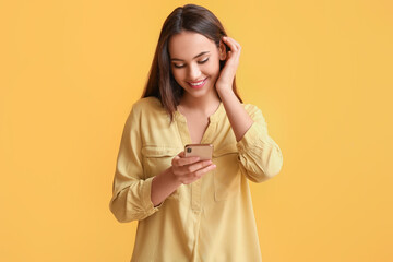 Beautiful young woman with mobile phone on yellow background
