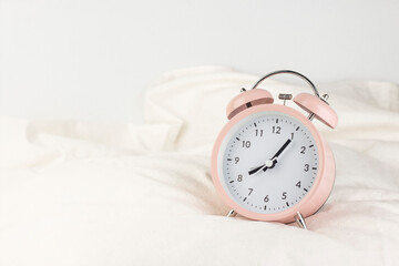 Morning concept. Classic pink alarm clock on the white wrinkled bed sheets close up image.