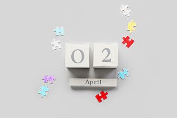 Cube calendar with date of World Autism Awareness Day and puzzle pieces on light background