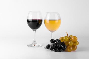 Two glasses of red and white wine and grapes on white background.