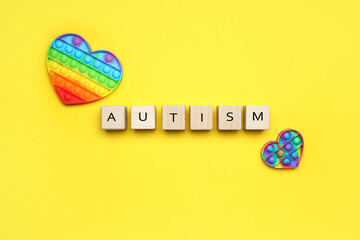 Wooden cubes with word AUTISM and pop it fidget toys on yellow background - obrazy, fototapety, plakaty