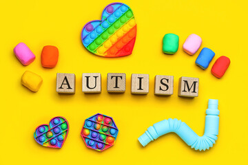 Wooden cubes with word AUTISM, toys and plasticine on yellow background