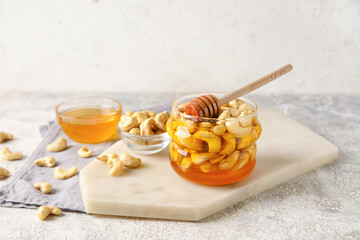 Board with jar of sweet cashew nuts in honey on grunge background