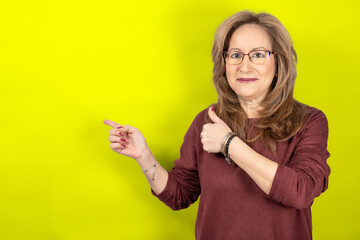 Woman pointing empty space and thumb up with smiling face, yellow studio background.