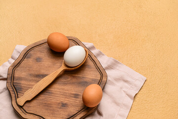 Wooden board with fresh chicken eggs on beige background