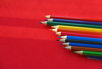 Multicolored pencils on a red background in the light