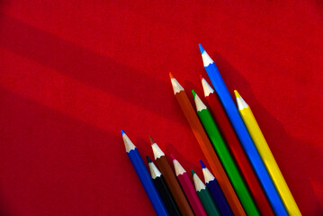 Multicolored pencils on a red background in the light