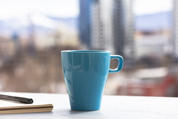 A cup of coffee, notebook, diary, a pencil, Workplace area and blurry urban view, Selective focus, copy space. Start of working day in a city concept