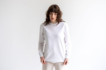 Young woman with curly hair in a white long sleeve t-shirt stands on a white background. Mock-up.