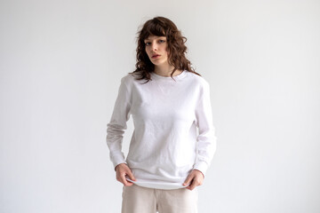 Young woman with curly hair in a white long sleeve t-shirt stands on a white background. Mock-up.