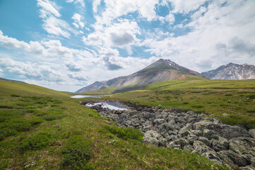 Scenic alpine landscape with two mountain lakes in sunlit mountain valley under cloudy sky. Dramatic sunny scenery with clouds reflection in water mirror of small lake among lichen stones in sunlight.