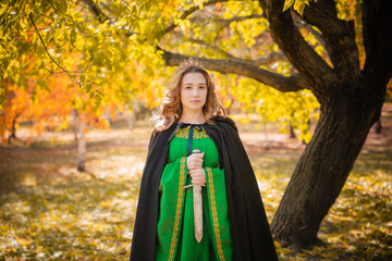 A beautiful girl in a medieval green dress with gold braid holds a dagger in her hands. Queen in a...