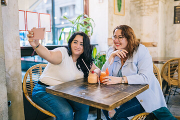 Happy plus size ladies taking selfie in cafe