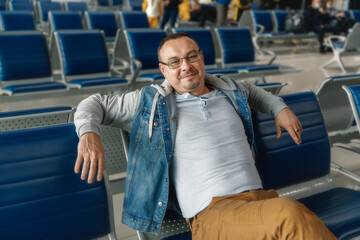 Traveler tourist man waiting to board into airplane, sitting in departure terminal in airport. Male passenger traveling by plane.