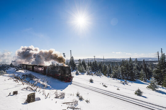 Brockenbahn historische Dampflokomotive mit viel Dampf im Winter in den Bergen mit verschneiten B&auml;umen 
