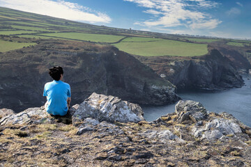 A man sitting on a rocky ridge, Boscastle, Cornwall, UK.