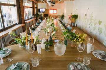 Coziness and style. Modern event design. Table setting at wedding reception. Floral compositions with beautiful flowers and greenery, candles, laying and plates on decorated table.