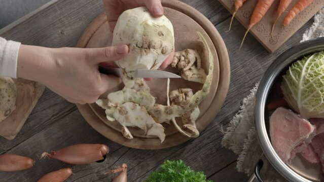 Hands peeling fresh celeriac - preparation of homemade broth or soup from beef marrow bones and vegetables
