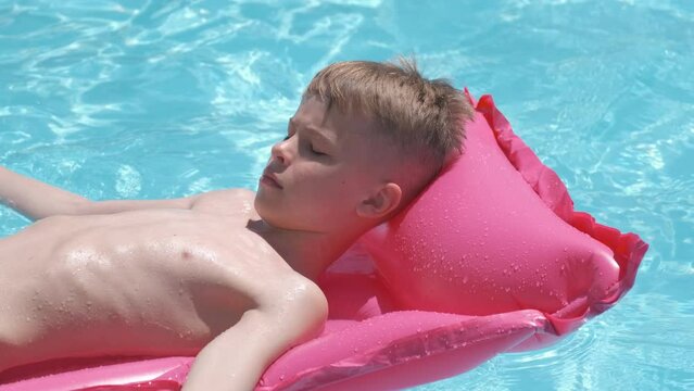 Young joyful child boy having fun swimming on inflatable air mattress in swimming pool with blue water on warm summer day on tropical vacations. Summertime activities concept