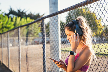 Young sport woman using black wireless headphones and setting a music playlist on her smartphone before working out.