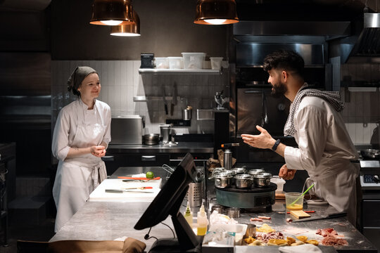 Happy Cooks Discussing Work In Restaurant Kitchen