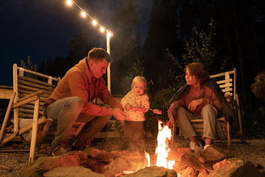 Parents helping baby to fry sausage on fire