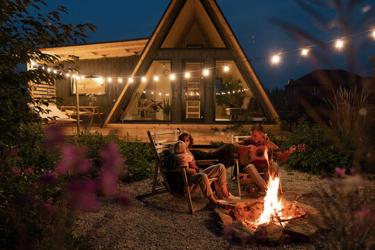 Parents with baby chilling near bonfire in backyard